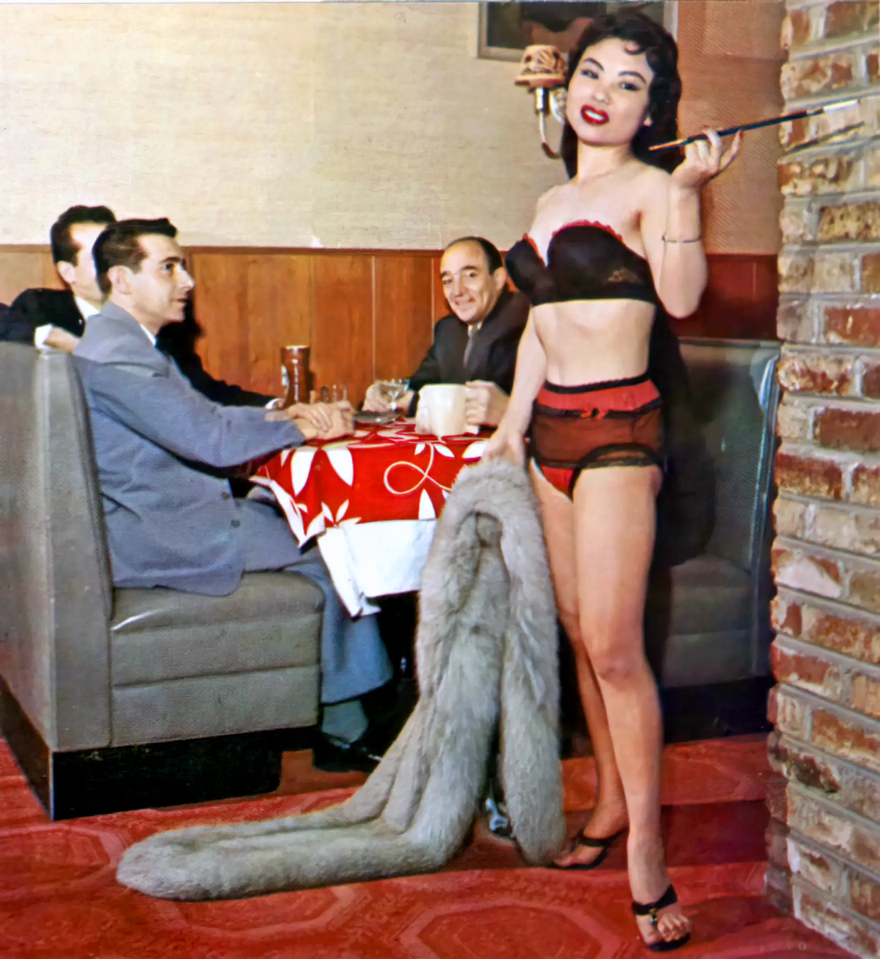 Burlesque brunette holds a long cigarette in a company of gentlemen