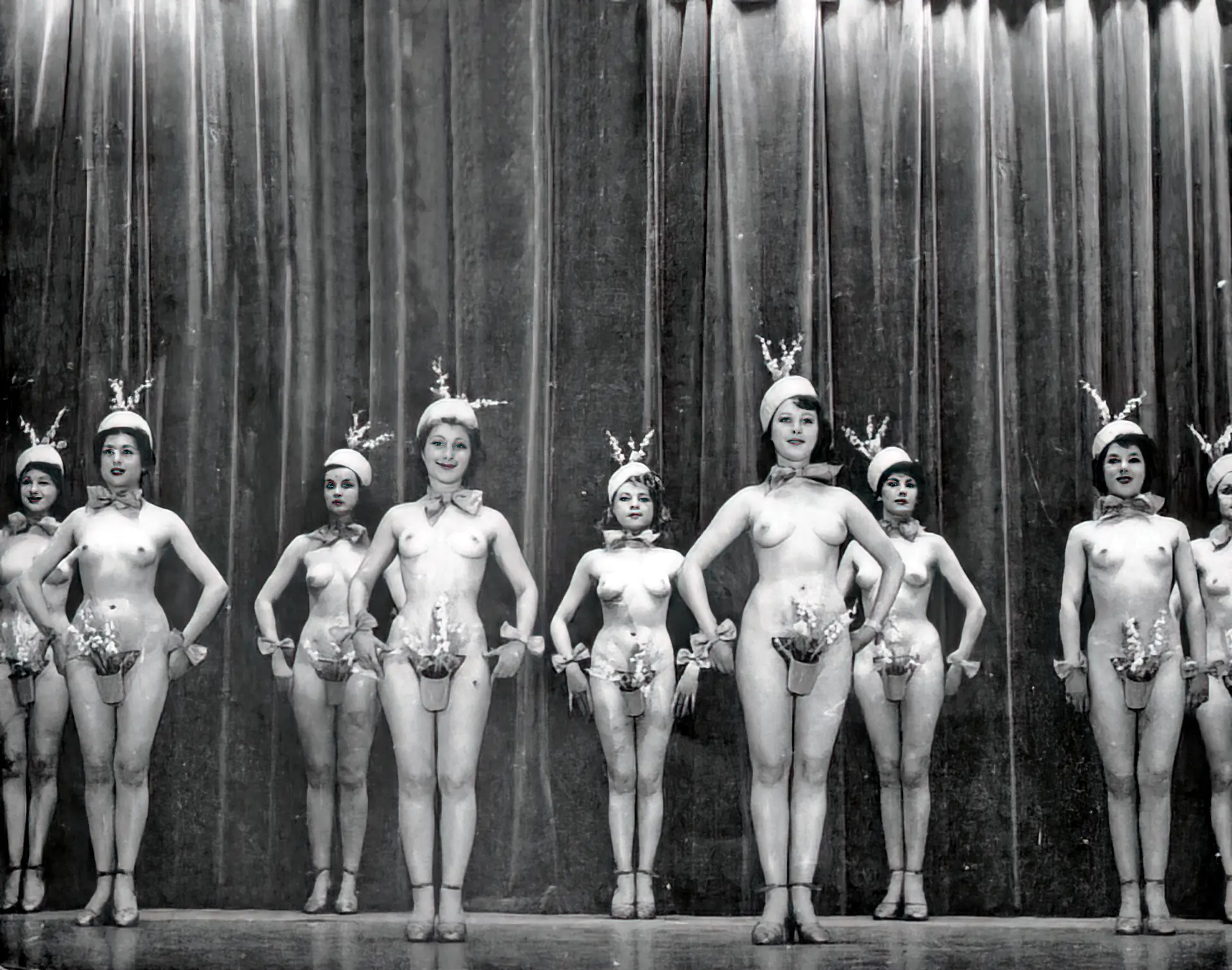 Burlesque girls stand topless on the stage with their pussies covered