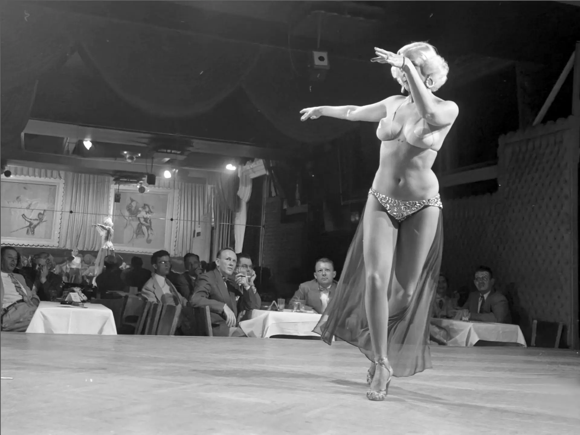 Curvy burlesque blonde dances on the stage for a bunch of men
